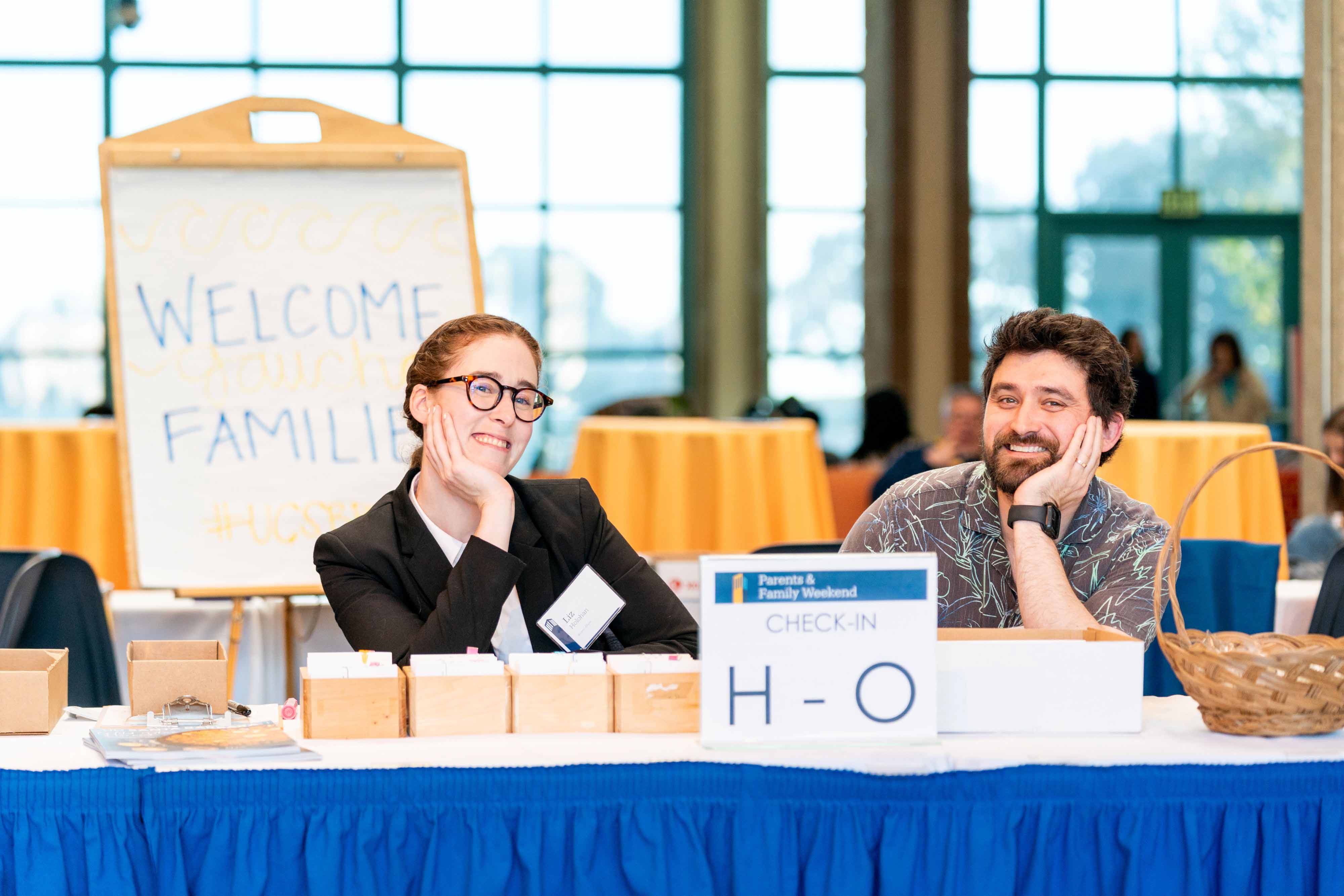 two staff members sitting at a booth for parents and family weekend
